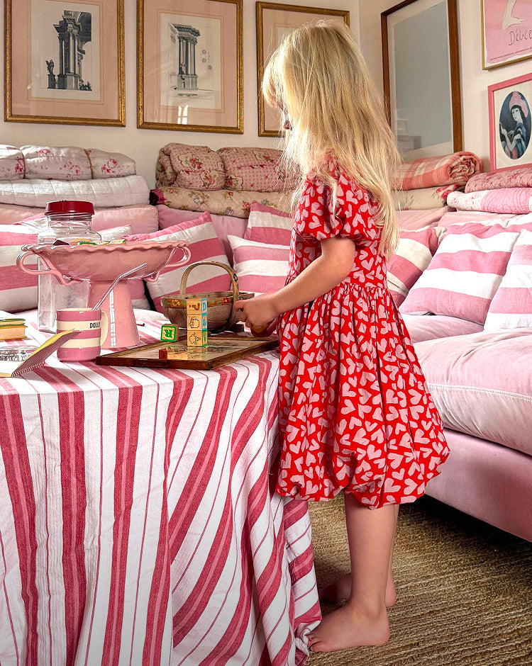 Young girl in a red dress playing with toys in a room with pink and white decor.