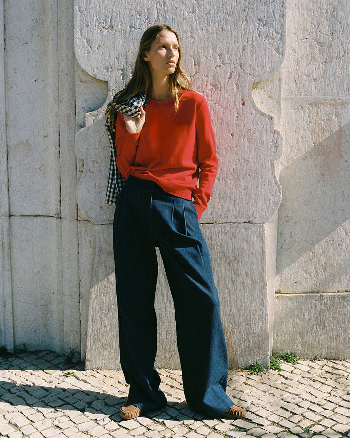 Woman in red sweater and blue jeans standing against a stone wall.