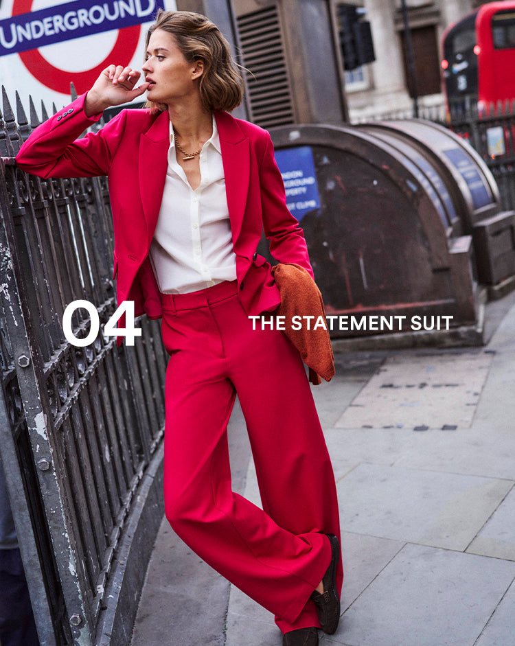 Woman in a red suit standing next to a London Underground sign.