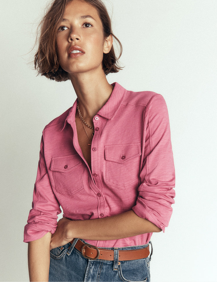 Woman wearing a pink shirt and jeans against a plain background
