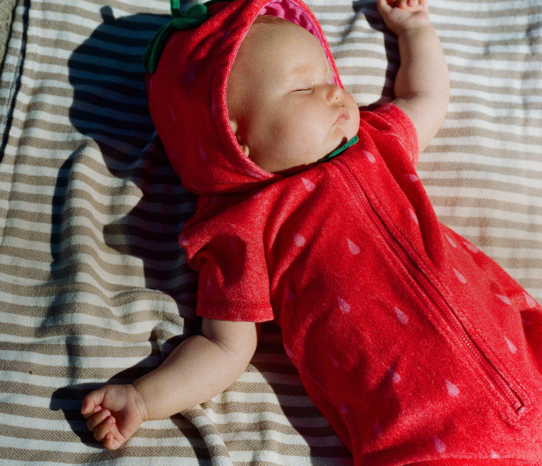 Baby wearing a red strawberry costume lying on a striped blanket