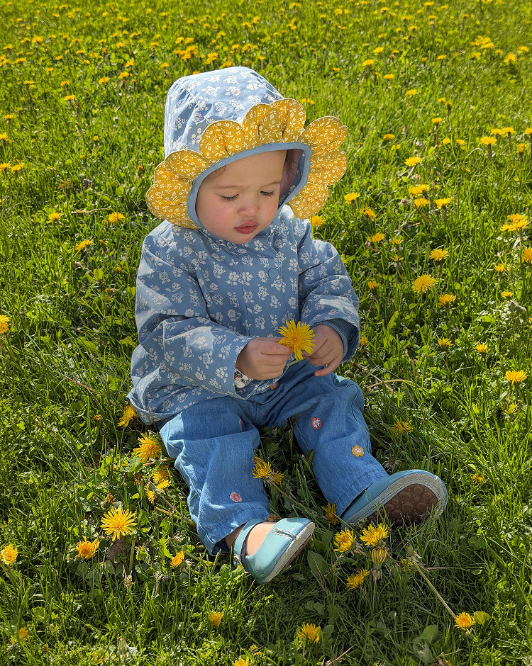 Child in a floral outfit and sun hat sitting in a field of dandelions