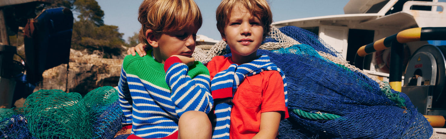 Two boys sitting on fishing nets wearing Boden sweaters.