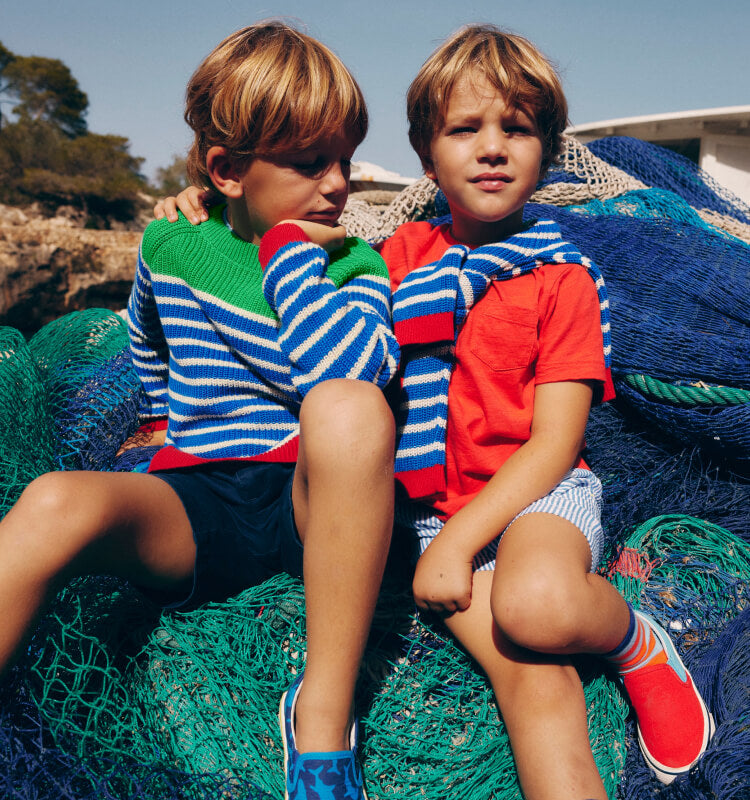 Two boys sitting on fishing nets wearing Boden sweaters.