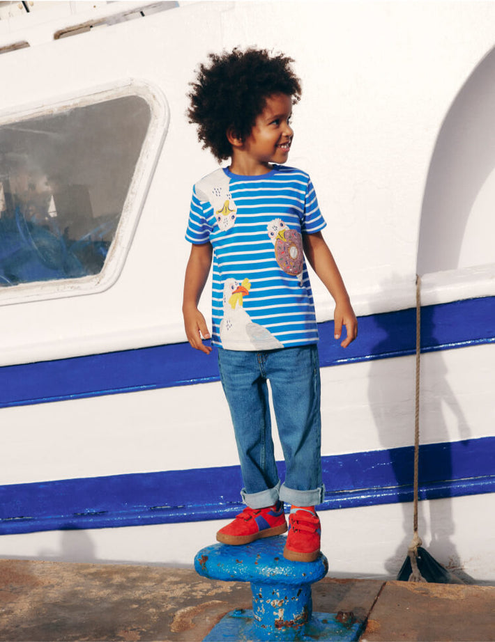 Boy standing next to a boat. Image link to Short Sleeve Appliqué T-shirt.