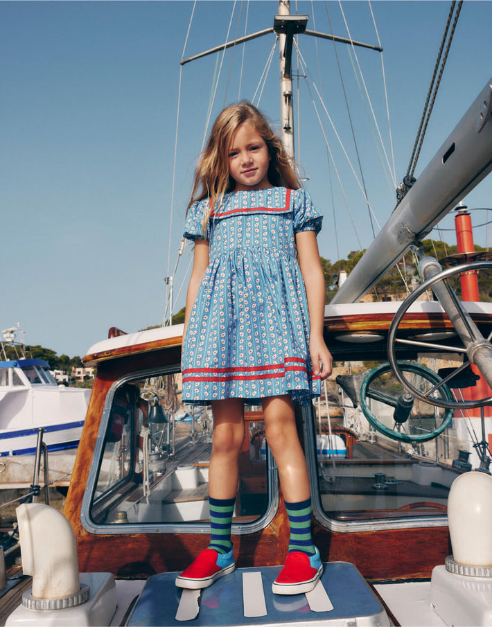 Girl wearing Boden dress on a boat, linking to Heritage Sailor Dress - Arctic Blue Daisy Stripe