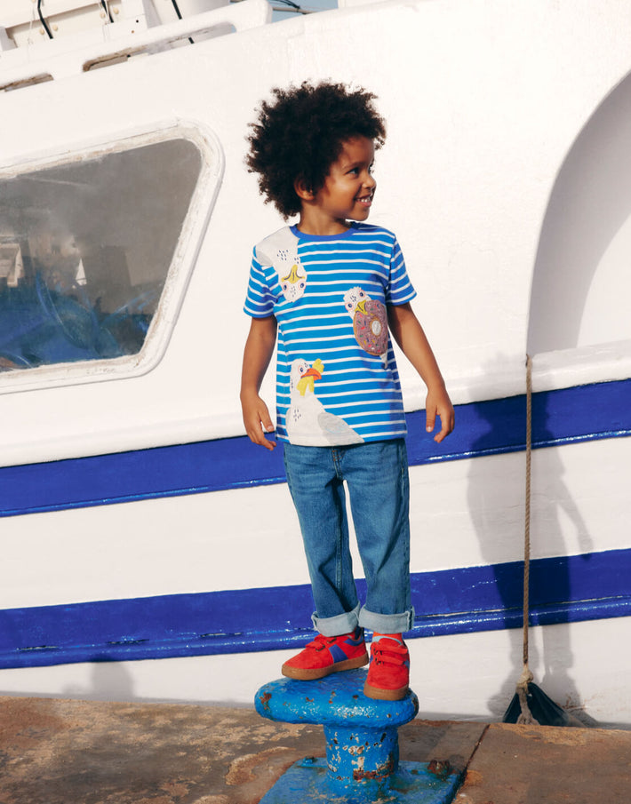 Boy by a boat wearing Boden, linking to Short Sleeve Applique T-Shirt - Gallery Blue Stripe Seagulls