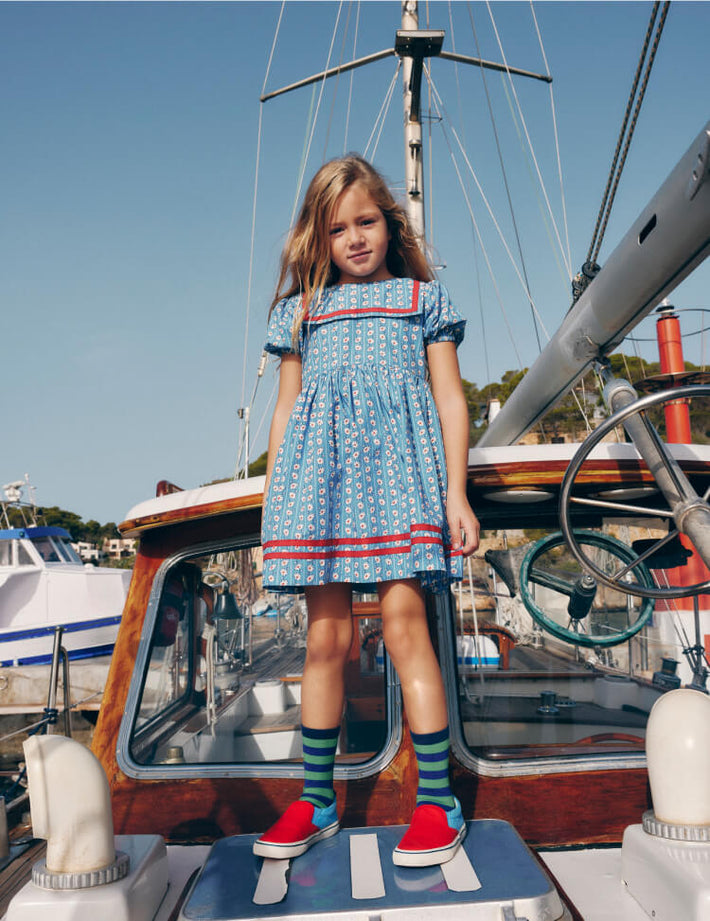 Girl wearing Boden dress on a boat, linking to Heritage Sailor Dress - Arctic Blue Daisy Stripe