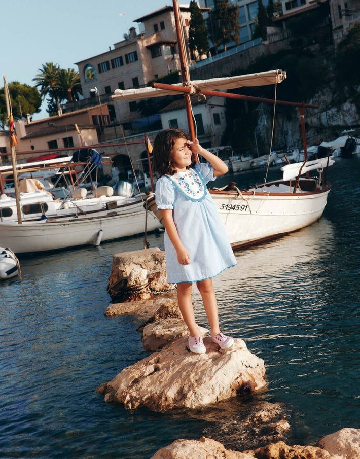 Girl standing on a rock in the sea. Image linking to Embroidered Yoke Dress.