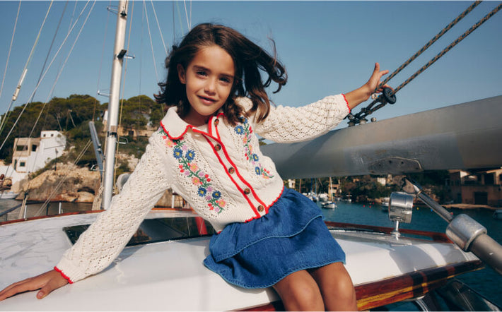 Girl sitting on a boat in Boden cardigan. Image link to Cotton Embroidered Cardigan.