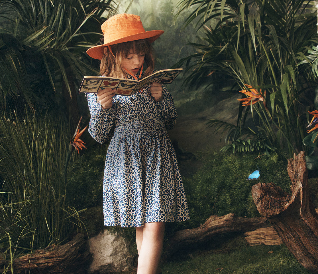 Child in a leopard print dress and orange hat reading a book in a jungle setting