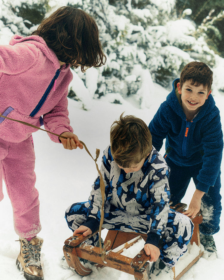 Three children playing in the snow with a wooden sled.