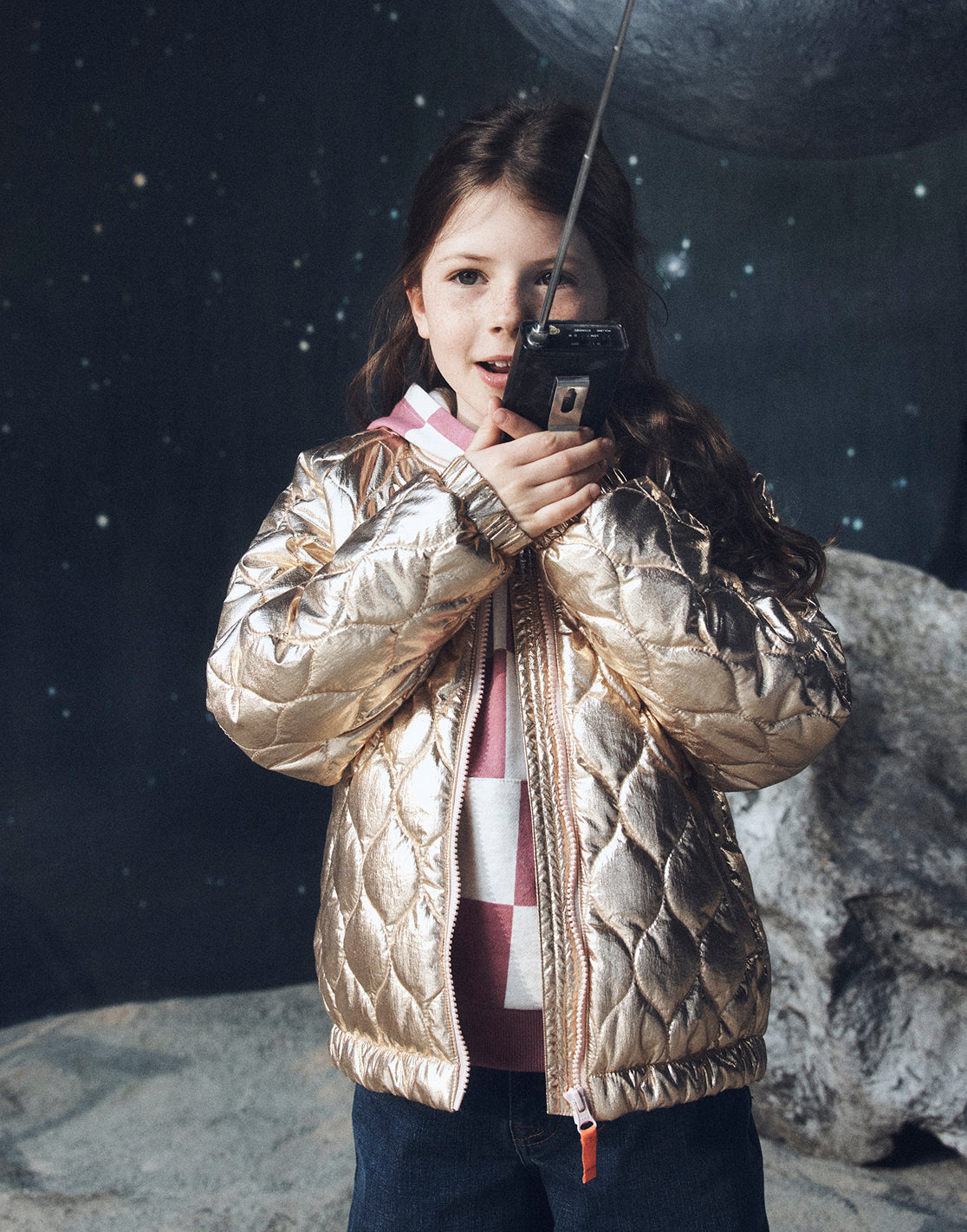 Child in a gold puffer jacket taking a selfie with a camera on a moon-like surface.