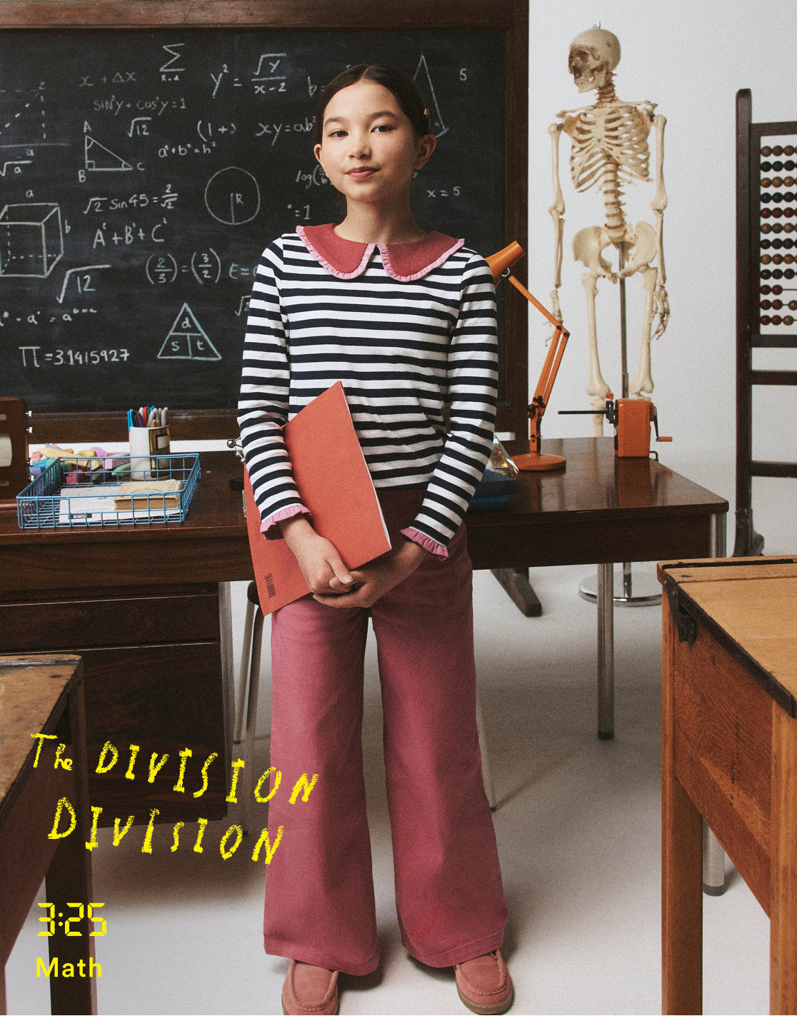 Young girl in a classroom setting holding a red book, with educational items like a blackboard and skeleton model in the background.