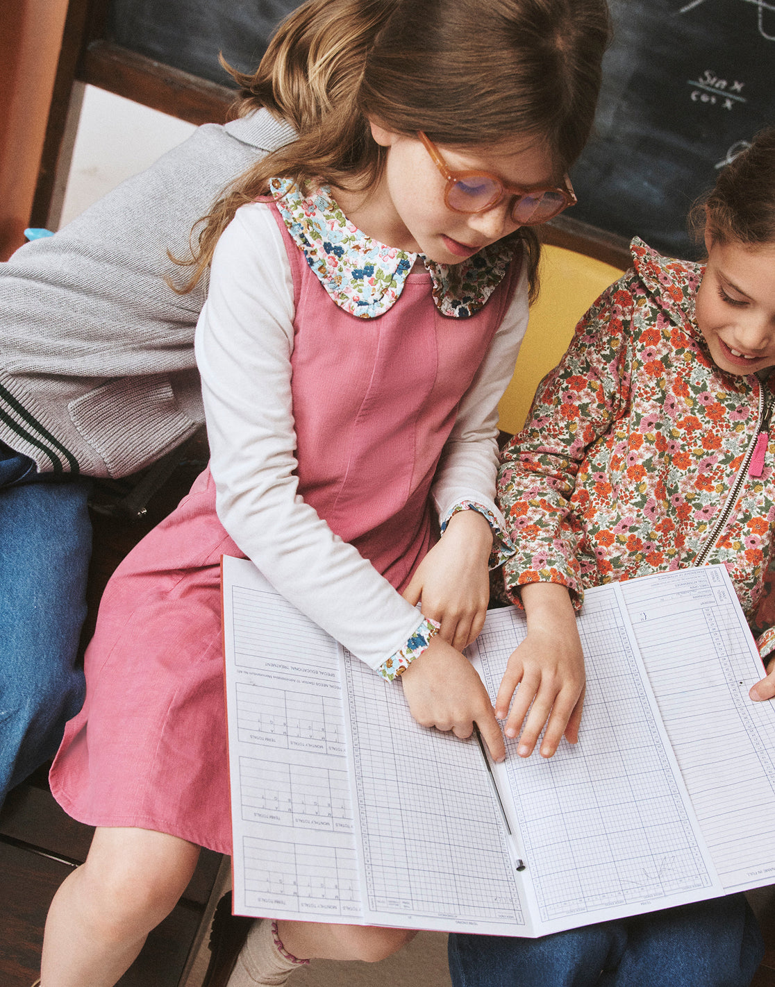 Two young girls looking at a book together in a classroom setting.