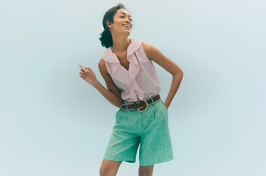 Woman wearing a pink blouse and green shorts against a light blue background