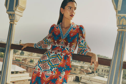 Woman in a colorful dress standing on a balcony with a cityscape in the background