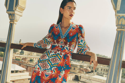 Woman in a colorful dress standing on a balcony with a cityscape in the background