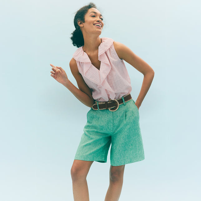 Woman wearing a pink blouse and green shorts against a light blue background