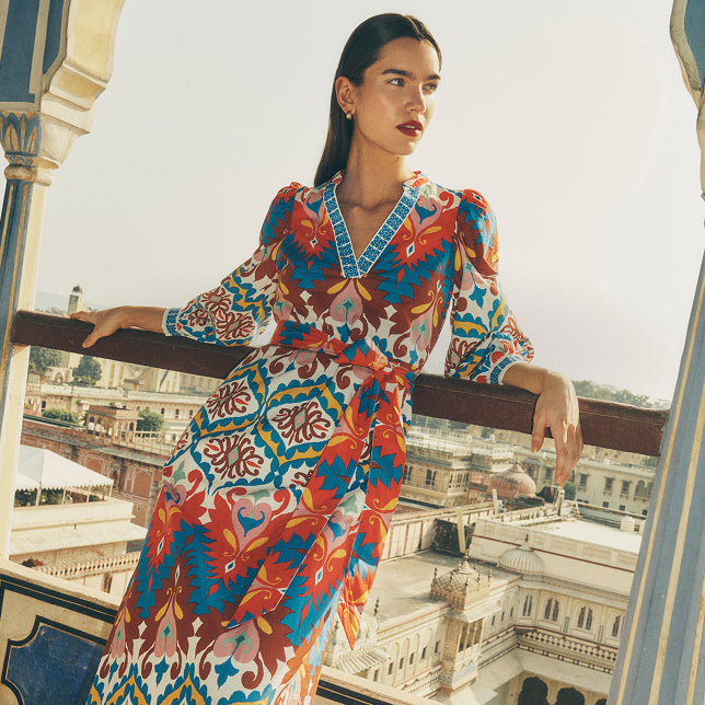 Woman in a colorful patterned dress standing on a balcony with a cityscape in the background