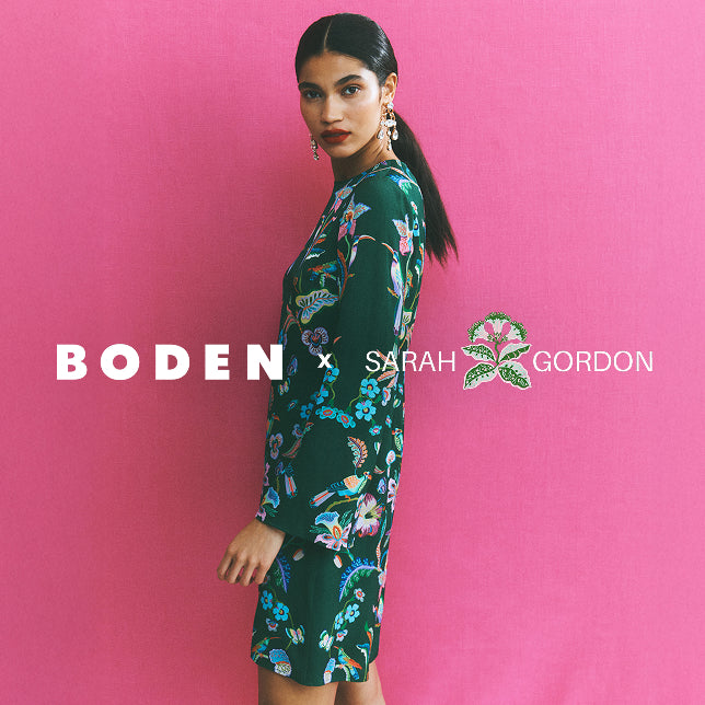 Woman wearing a floral dress with 'Boden x Sarah Gordon' branding on a pink background